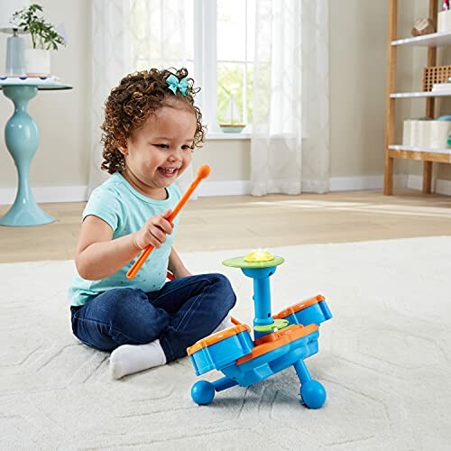 Toddler happily playing with a colorful toy drum set on the floor.